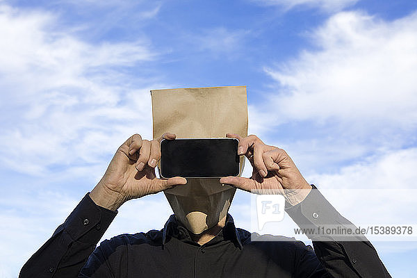 Mann mit Papiertüte über dem Kopf und Handy