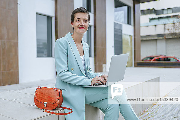Frau in Anzugsjacke benutzt Laptop im Freien