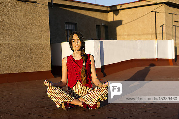 Teenagerin meditiert bei Sonnenuntergang auf der Dachterrasse