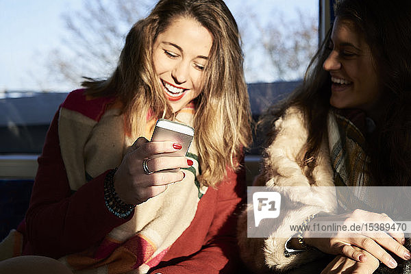 UK London two happy women in underground train using cell phone