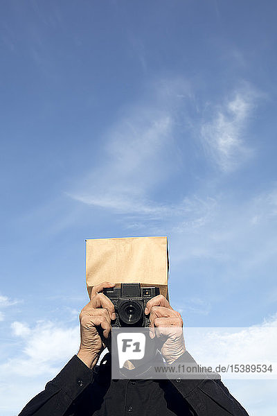 Man with paper bag above his head taking a picture