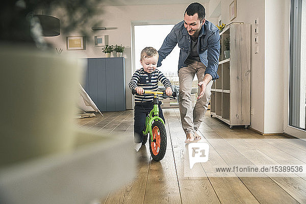 Vater hilft Sohn beim Fahren mit einem Balance-Fahrrad zu Hause