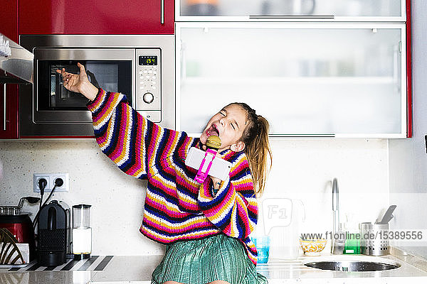 Mädchen spielt mit Mikrofon und Smartphone in der heimischen Küche