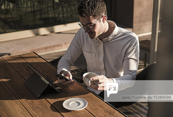 Young man using cell phone and tablet at outdoor cafe
