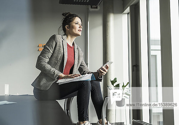 Businesswoman sitting on desk in office looking out of window