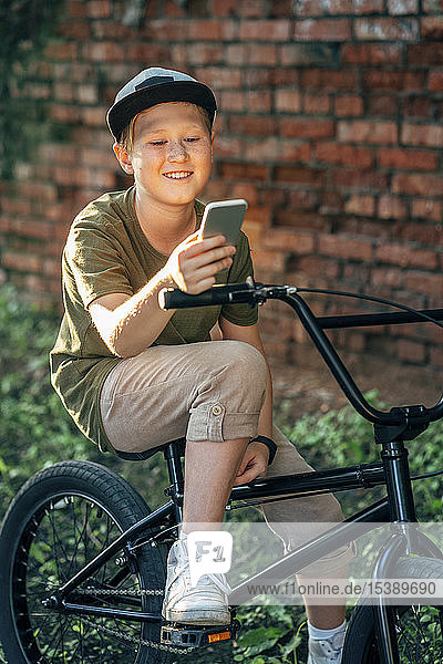 Smiling boy with bmx bike using cell phone
