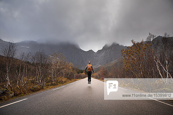 Norwegen Lofoten-Inseln Mann springt auf leere Straße umgeben von einer Felswand