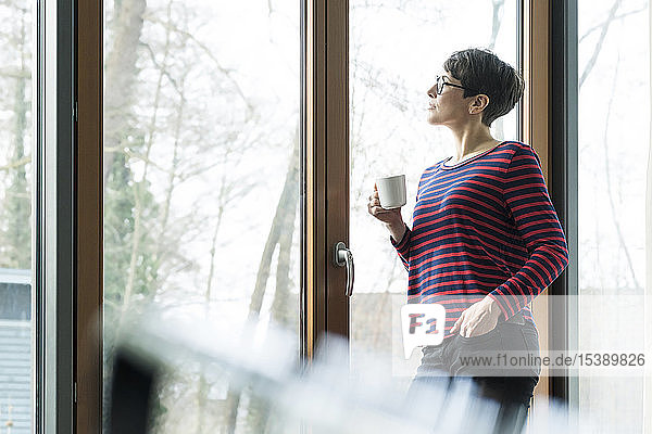 Frau mit Kaffeetasse  die aus der Terrassentür schaut