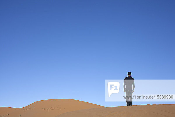 Morocco  Merzouga  Erg Chebbi  rear view of man wearing a bowler hat standing on desert dune