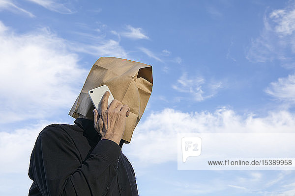 Man with paper bag above his head talking on cell phone