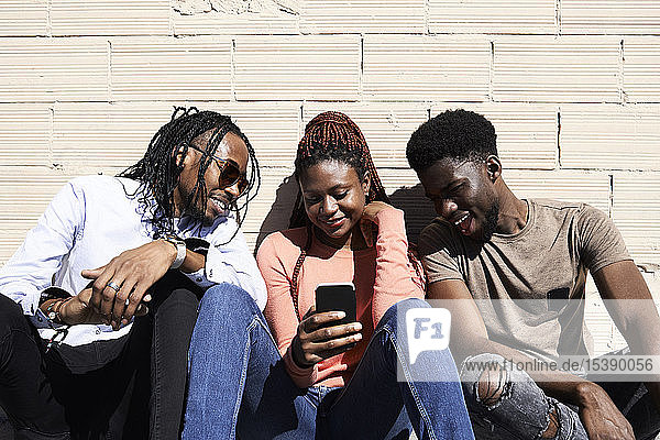 Drei Freunde sitzen zusammen und schauen sich im Freien ein Video auf einem Smartphone an