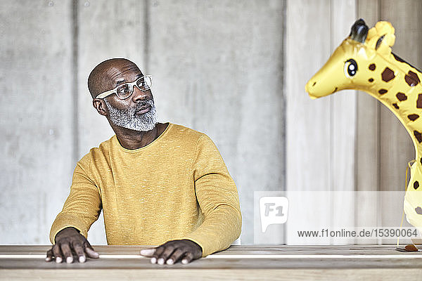 Überraschter reifer Geschäftsmann sitzt im Büro am Schreibtisch und betrachtet Giraffenfigur
