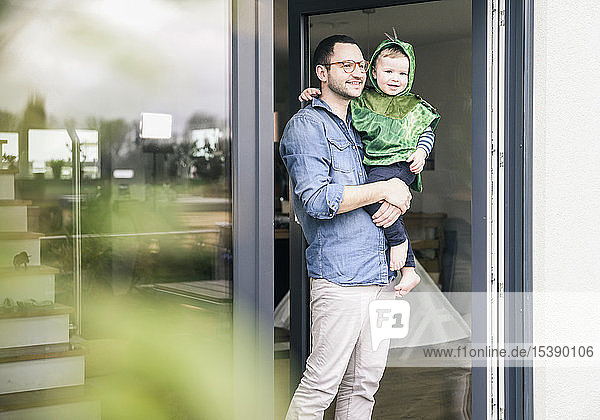 Vater trägt Sohn in einem Kostüm an Terrassentür zu Hause