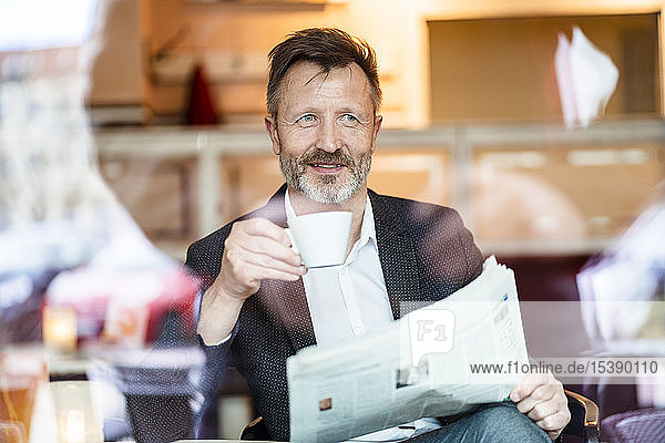 Porträt eines lächelnden reifen Geschäftsmannes mit Zeitung  der in einem Café sitzt und Kaffee trinkt