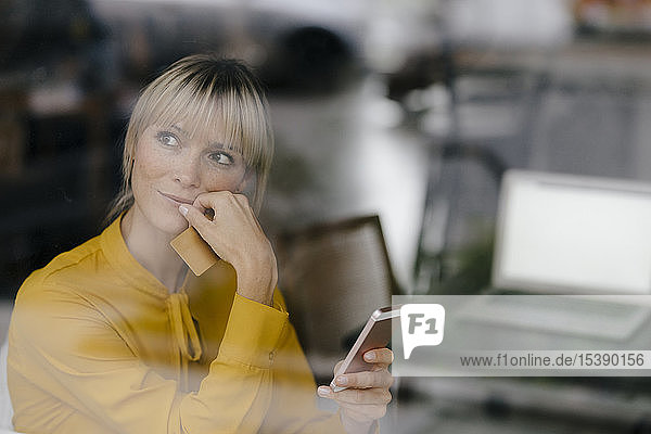 Blond businesswoman sitting at window  doing a paymant with smartphone and creditcard