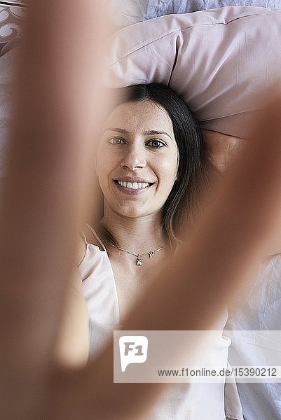 Porträt einer lächelnden  auf dem Bett liegenden jungen Frau mit Siegeszeichen  Draufsicht