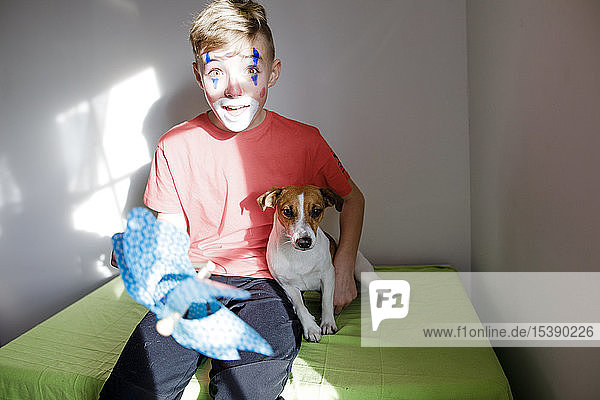 Portrait of amazed boy made up as a clown with dog and pin wheel at home