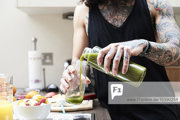 Tattooed young man pouring in healthy smoothie in kitchen