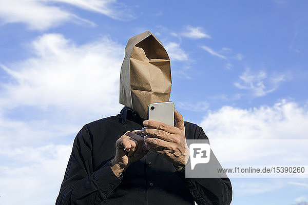 Man with paper bag above his head using cell phone