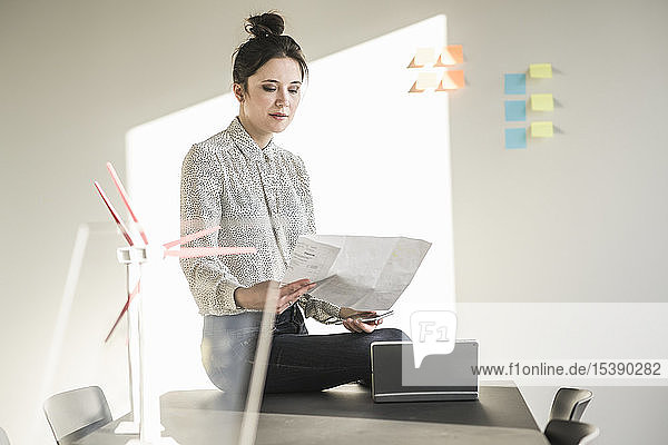 Businesswoman in office reading plan with wind turbine models on desk