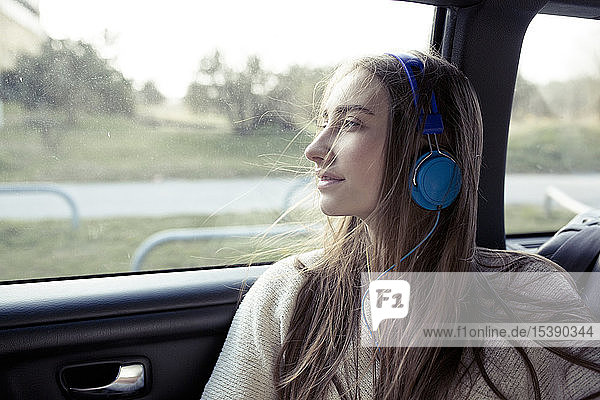 Young woman with windswept hair in a car wearing headphones