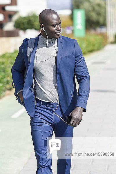 Geschäftsmann im blauen Anzug  der mit Kopfhörern und Smartphone Musik hört