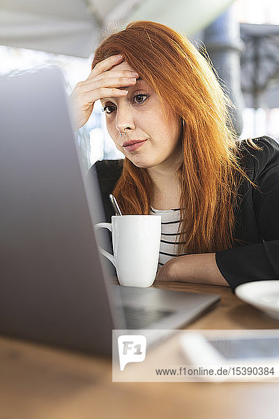 Porträt einer rothaarigen jungen Frau  die im Straßencafé auf den Laptop schaut