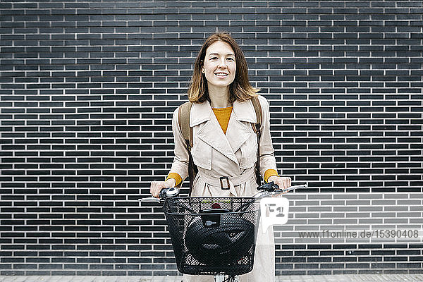 Porträt einer lächelnden Frau mit E-Bike an einer Ziegelmauer