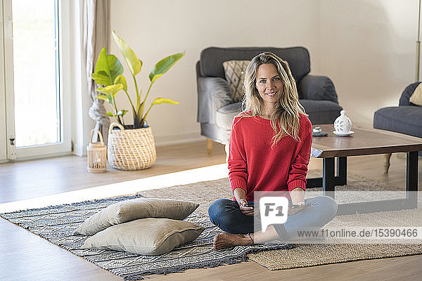 Porträt einer lächelnden Frau  die zu Hause auf dem Boden sitzt und ein Tablett hält