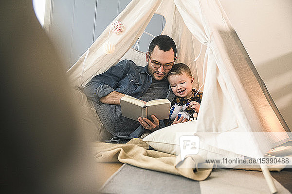 Father and son reading a book together in tent at home