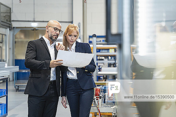Businessman and businesswoman looking at plan in factory