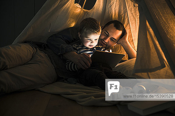 Father and son sharing a tablet in a dark tent at home