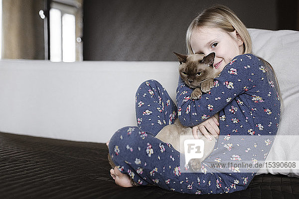 Bildnis eines lächelnden kleinen Mädchens in Pyjama mit Blumenmuster  das eine Katze hält