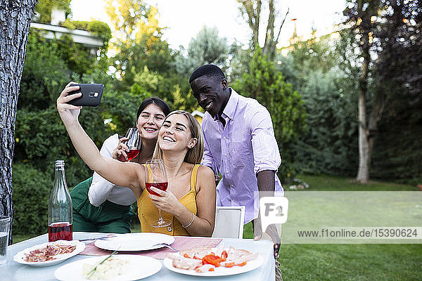 Freunde amüsieren sich bei einem sommerlichen Abendessen im Garten und nehmen sich selbst