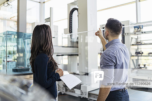 Rückansicht eines Geschäftsmannes und einer Geschäftsfrau im Gespräch in einer modernen Fabrik
