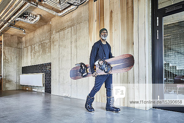 Mature businessman holding snowboard in modern office