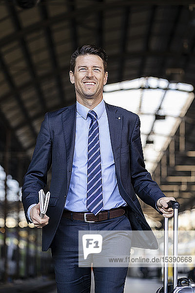Smiling businessman walking with suitcase on station platform