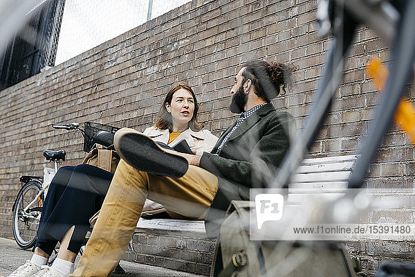 Ehepaar sitzt auf einer Bank neben E-Bikes und unterhält sich