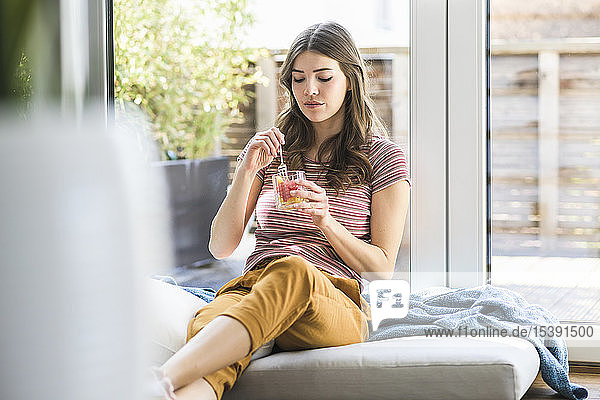 Junge Frau sitzt zu Hause am Fenster und isst einen Imbiss