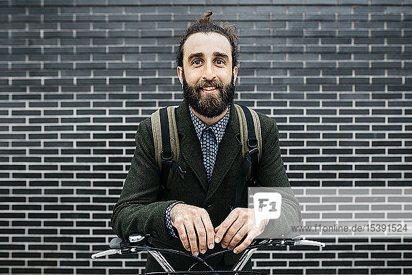 Porträt eines lächelnden Mannes mit E-Bike an einer Ziegelmauer