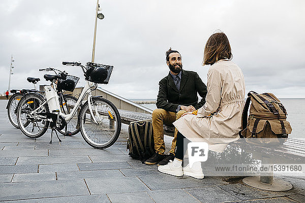 Ehepaar sitzt auf einer Bank an der Strandpromenade neben E-Bikes und unterhält sich