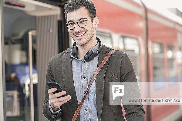 Lächelnder junger Mann mit Handy im Nahverkehrszug