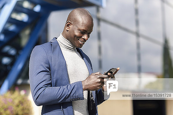 Lächelnder Geschäftsmann in blauem Anzug und grauem Rollkragenpullover schaut auf Handy