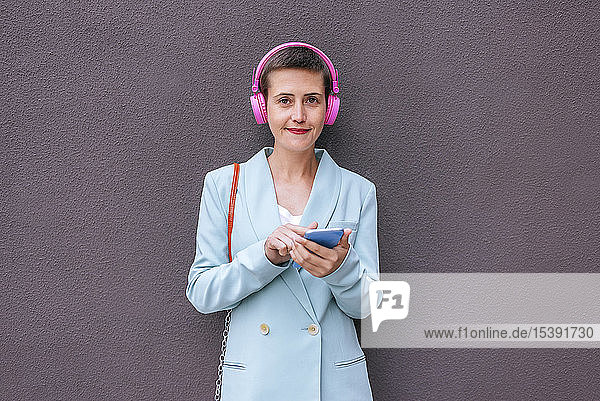 Frau in Jacke gekleidet  die mit ihrem Mobiltelefon Musik hört