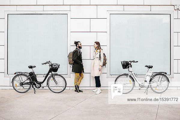 Mann und Frau mit E-Fahrrädern stehen vor einem Gebäude und unterhalten
