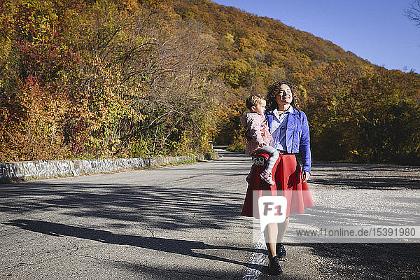 Mutter trägt ihre Tochter auf einer Landstraße