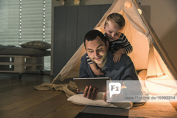 Father and son sharing a tablet at an illuminated tent at home