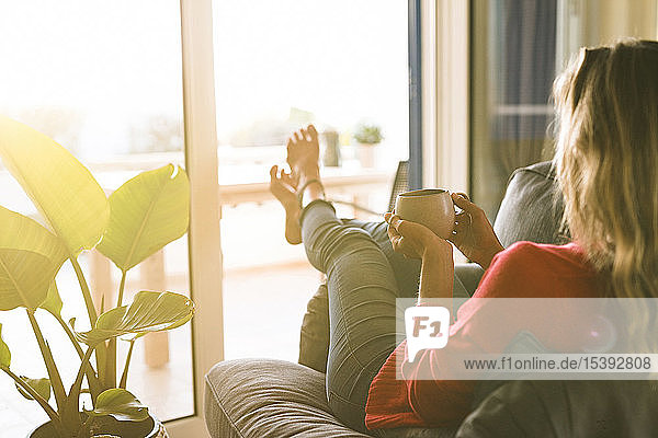 Frau entspannt sich zu Hause im Sessel und hält Kaffeetasse