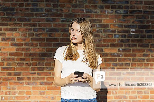 Young woman in front of brick wall  using smartphone