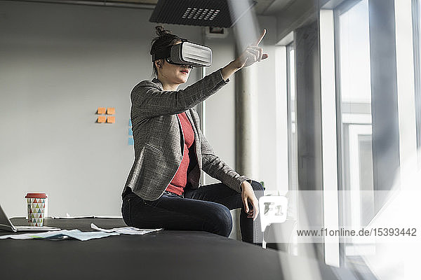 Geschäftsfrau  die mit einer VR-Brille auf dem Schreibtisch im Büro sitzt